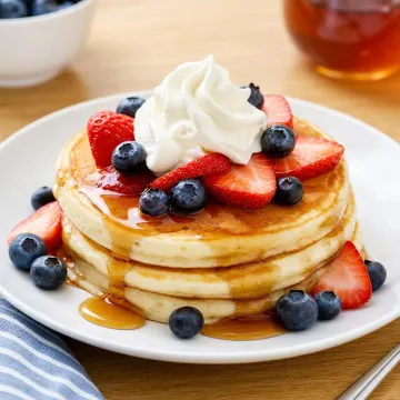 Panqueques servidos con miel, frutas frescas y crema batida