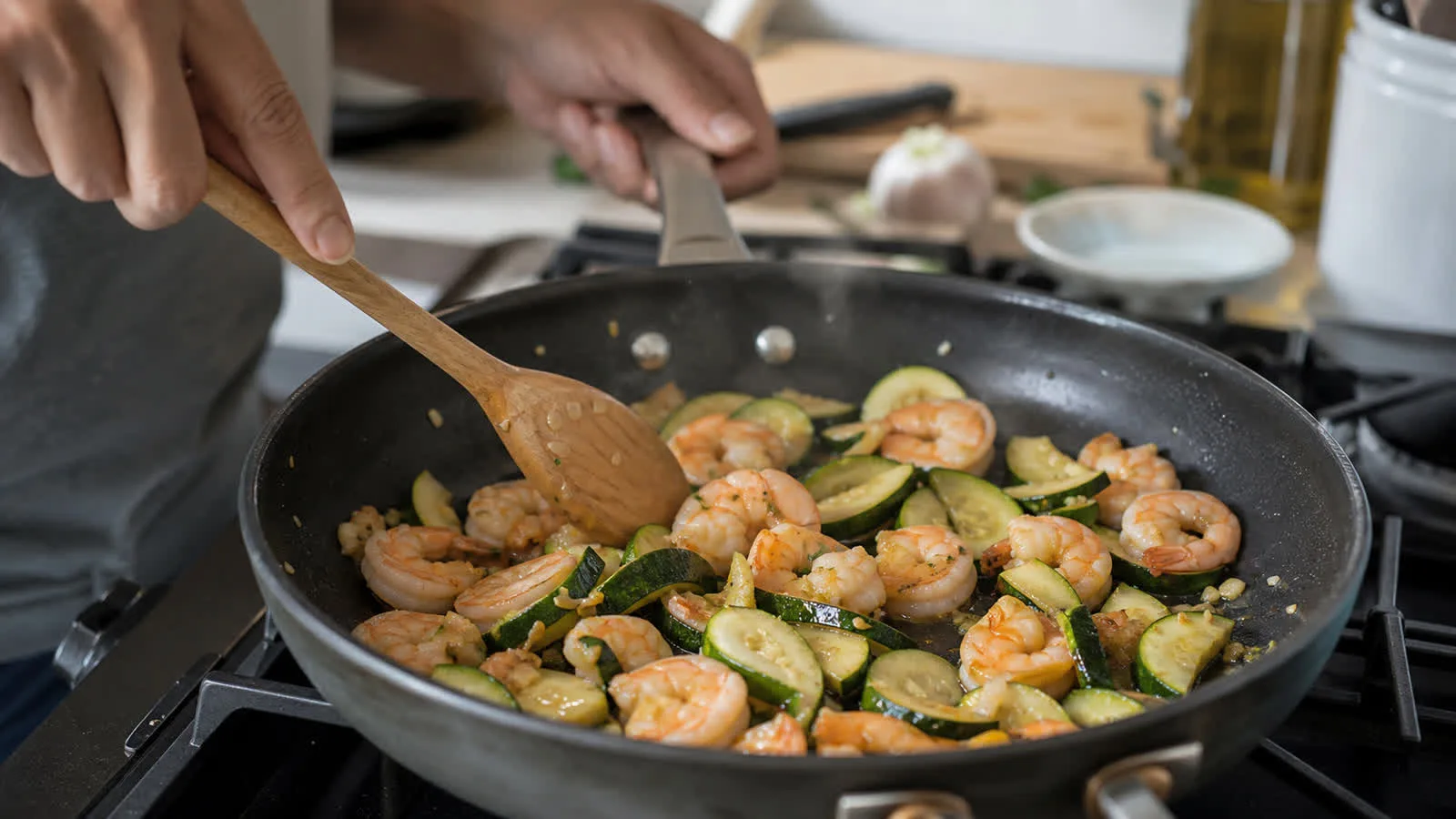 Manos cocinando camarones con calabacitas y ajo en sarten casero