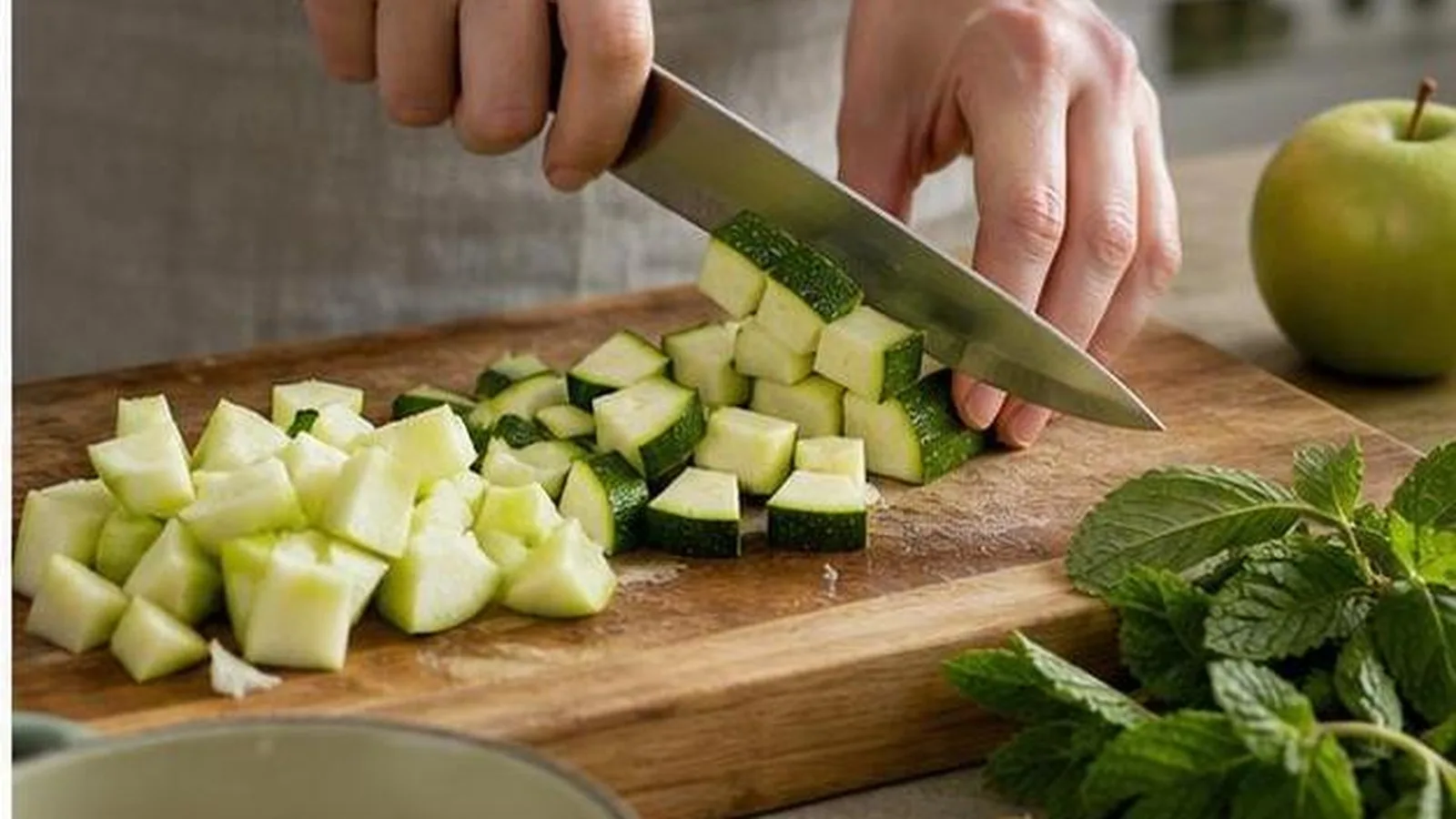 Manos cortando calabacin y manzana verde para una crema casera con menta