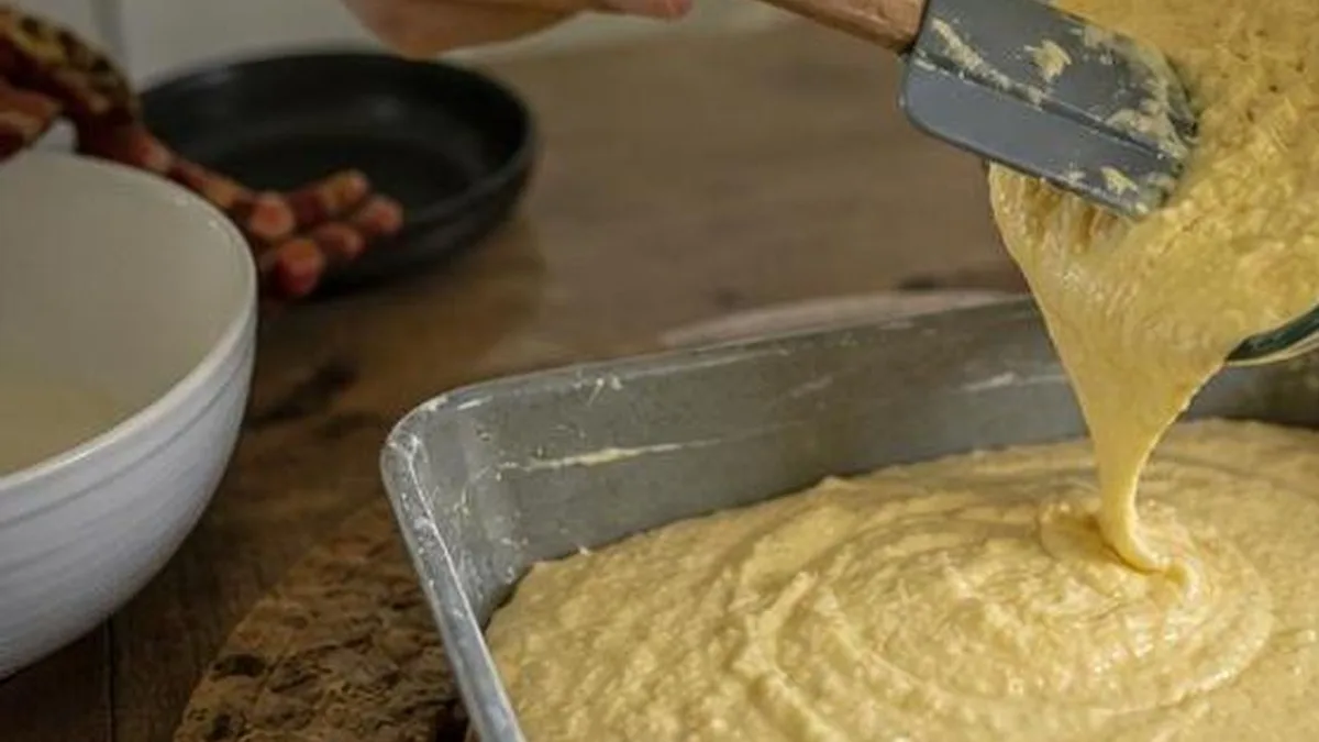 Manos vertiendo mezcla de pastel de elote en un molde para hornear