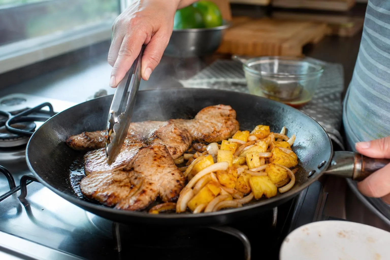 Manos cocinando chuletas de cerdo con piña en sartén casero