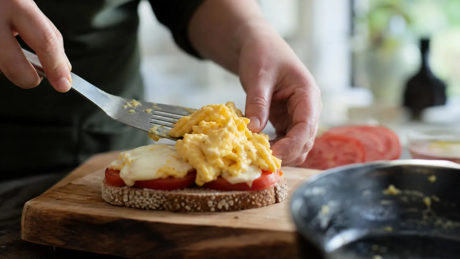 Manos armando sándwiches calientes con huevo, queso y jitomate sobre pan en cocina casera