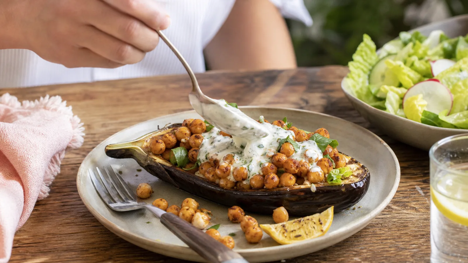 Berenjenas asadas con garbanzos especiados servidas con salsa de yogur en mesa casera