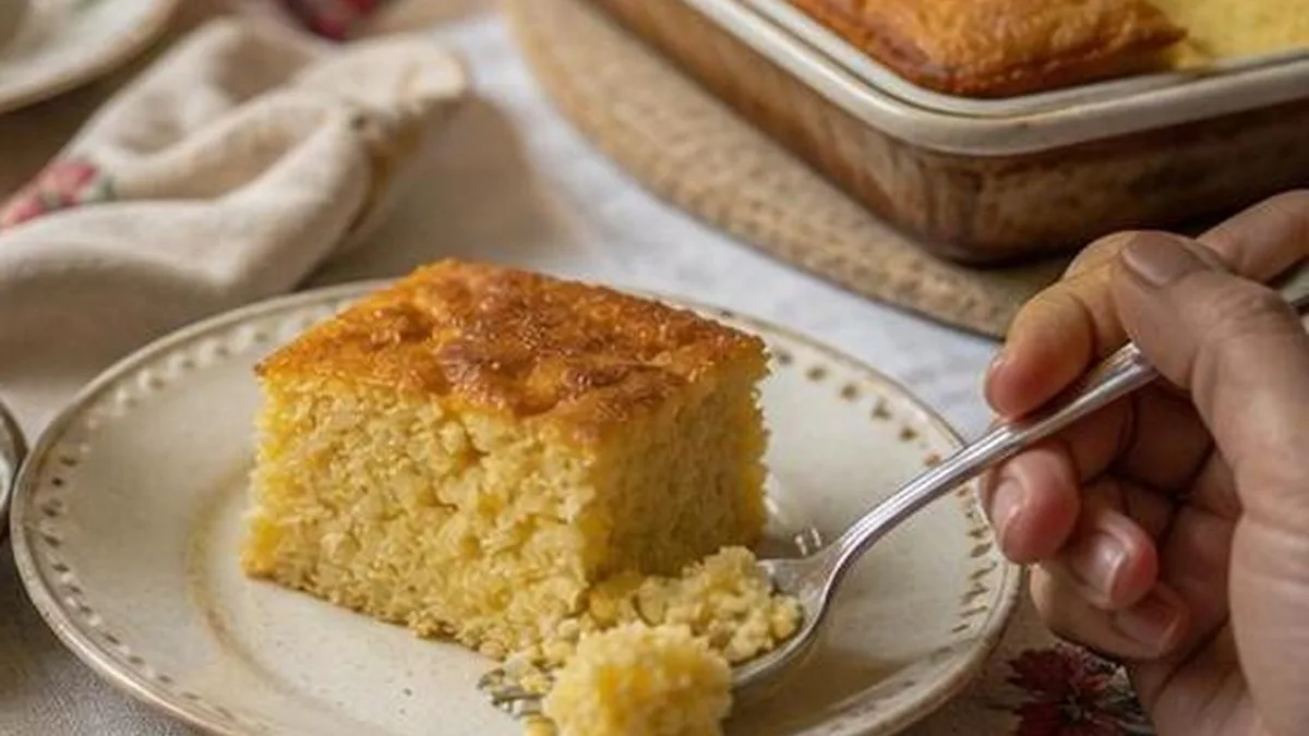 Rebanada de pastel de elote con queso crema servida en plato con café