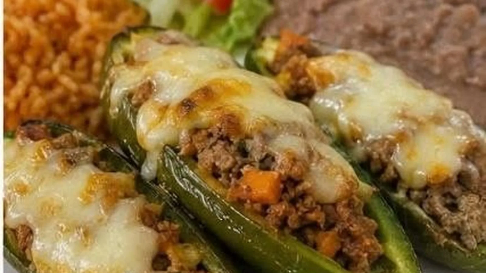 Chiles jalapenos rellenos de picadillo con queso gratinado servidos con arroz y frijoles